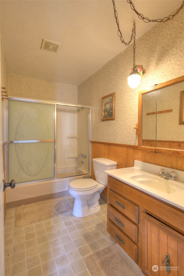 full bathroom with shower / bath combination with glass door, wood walls, vanity, and toilet