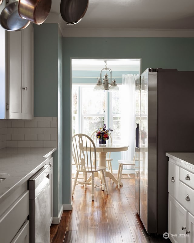 kitchen with white cabinetry, stainless steel appliances, light wood-type flooring, ornamental molding, and a notable chandelier