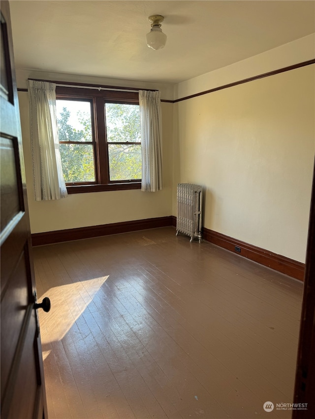 empty room with radiator heating unit and hardwood / wood-style flooring