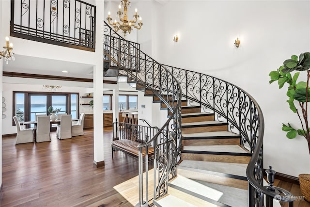 staircase featuring wood-type flooring, a notable chandelier, crown molding, and a high ceiling