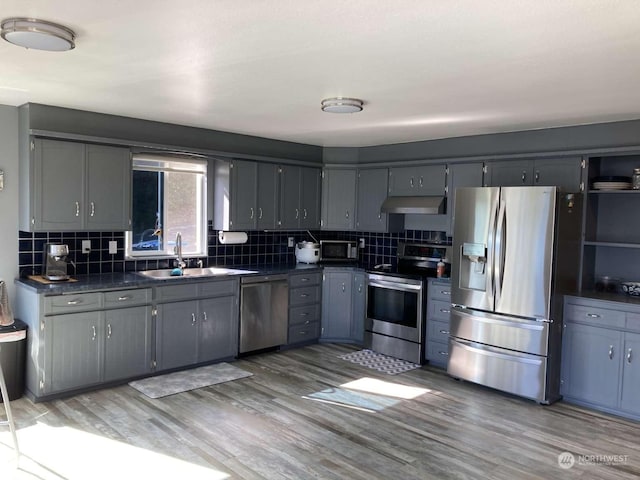 kitchen with light hardwood / wood-style floors, gray cabinets, stainless steel appliances, decorative backsplash, and sink