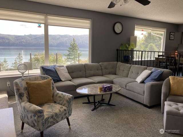 carpeted living room with a textured ceiling, a water and mountain view, a healthy amount of sunlight, and ceiling fan