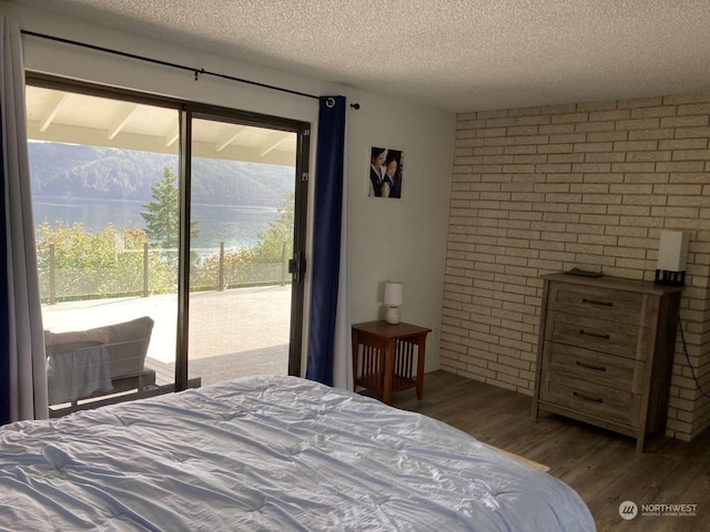 bedroom with a textured ceiling, brick wall, access to exterior, and hardwood / wood-style flooring