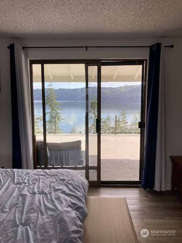 bedroom with access to exterior, wood-type flooring, and a water view