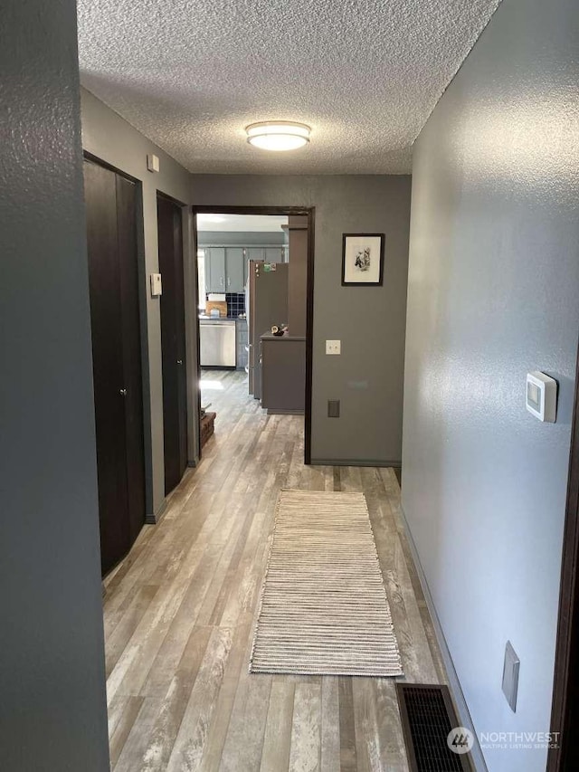 corridor featuring light wood-type flooring and a textured ceiling