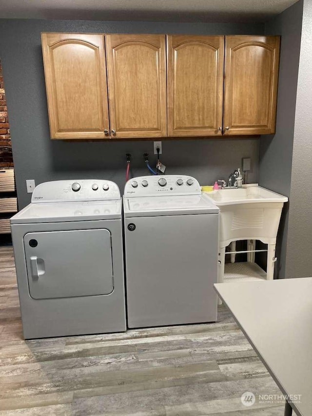 laundry room with light hardwood / wood-style flooring, separate washer and dryer, and cabinets