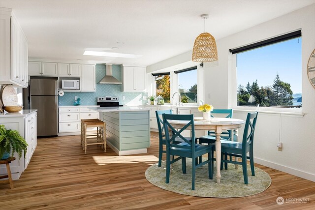 kitchen featuring appliances with stainless steel finishes, wall chimney range hood, white cabinets, and light hardwood / wood-style floors