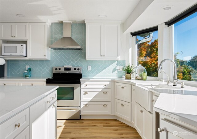 kitchen with tasteful backsplash, wall chimney range hood, white cabinetry, light hardwood / wood-style floors, and stainless steel electric range oven