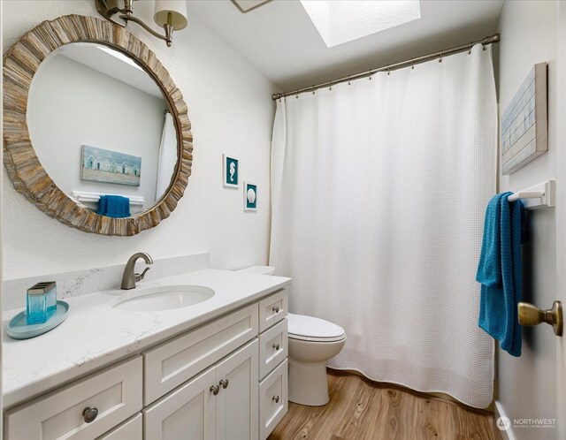 bathroom featuring vanity, toilet, wood-type flooring, and a skylight