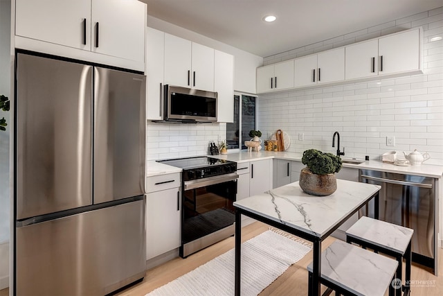 kitchen with light hardwood / wood-style floors, sink, stainless steel appliances, backsplash, and white cabinetry