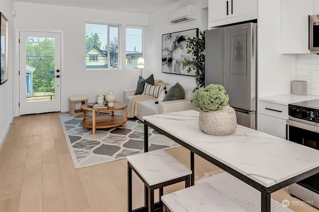 interior space featuring an AC wall unit, appliances with stainless steel finishes, light hardwood / wood-style flooring, and white cabinetry