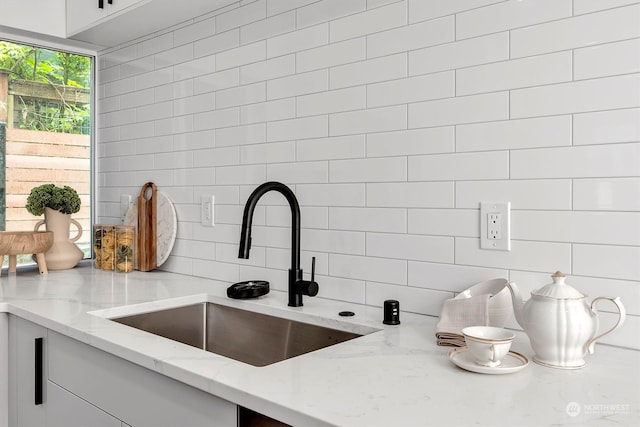 interior details featuring light stone counters, white cabinetry, sink, and backsplash