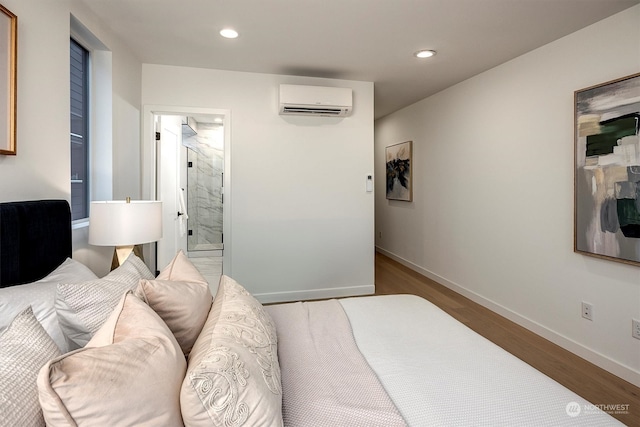 bedroom with a wall mounted AC, connected bathroom, and light wood-type flooring