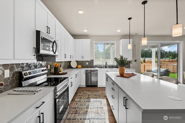 kitchen with pendant lighting, white cabinets, stainless steel appliances, and a healthy amount of sunlight