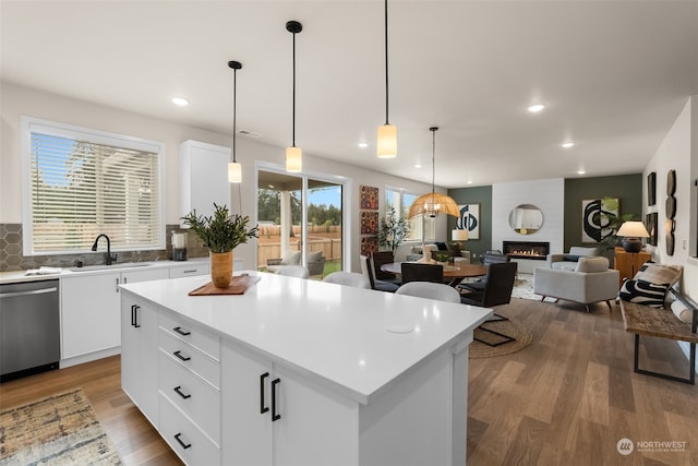 kitchen with a kitchen island, hardwood / wood-style floors, decorative light fixtures, stainless steel dishwasher, and white cabinetry