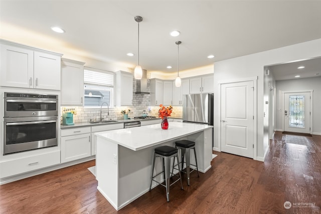 kitchen with dark wood-type flooring, stainless steel appliances, hanging light fixtures, a center island, and white cabinetry