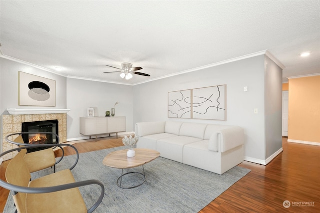 living room with ceiling fan, ornamental molding, a textured ceiling, a tiled fireplace, and hardwood / wood-style flooring