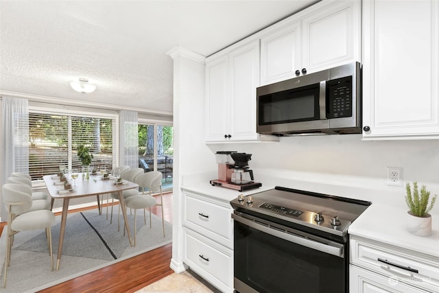 kitchen featuring stainless steel appliances, white cabinets, light hardwood / wood-style flooring, and a textured ceiling