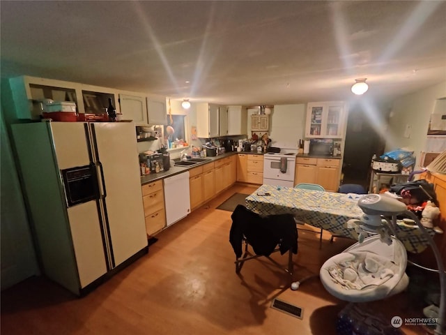 kitchen with visible vents, a sink, dark countertops, white appliances, and light brown cabinetry