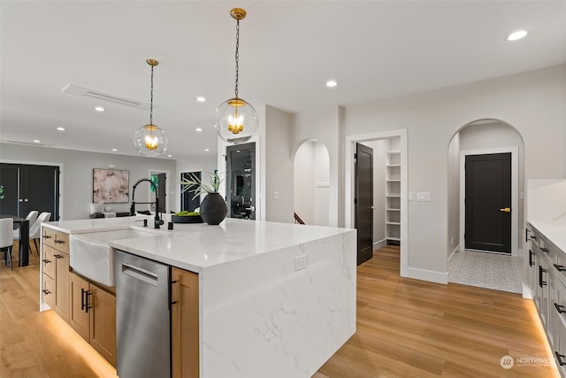 kitchen with dishwasher, a kitchen island with sink, decorative light fixtures, light wood-type flooring, and light stone counters