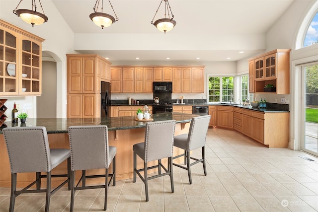 kitchen with pendant lighting, sink, black appliances, a kitchen breakfast bar, and dark stone counters