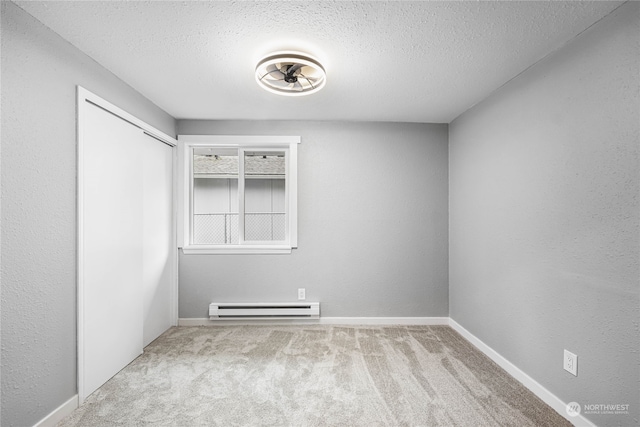 empty room with light colored carpet, a baseboard heating unit, and a textured ceiling