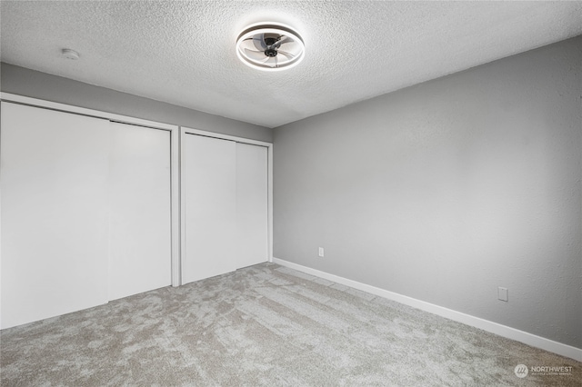 unfurnished bedroom with light carpet, multiple closets, and a textured ceiling