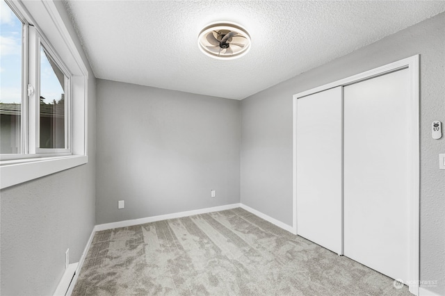 unfurnished bedroom featuring a textured ceiling, a closet, and light colored carpet