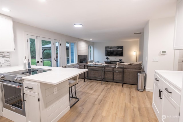 kitchen with white cabinetry, french doors, high end stainless steel range oven, a kitchen bar, and light wood-type flooring