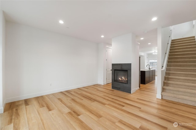 unfurnished living room featuring a multi sided fireplace, sink, and light wood-type flooring