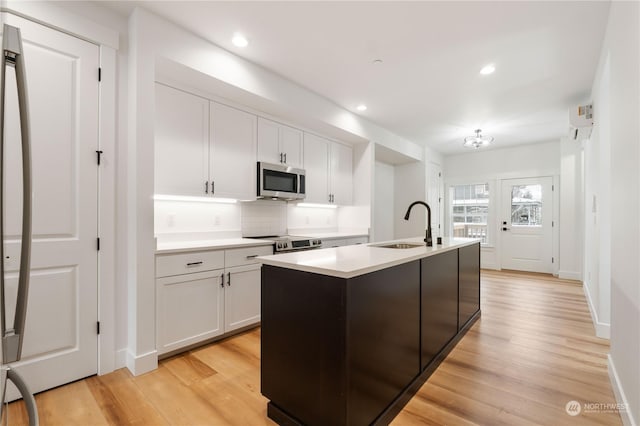 kitchen featuring white cabinetry, sink, stainless steel appliances, and an island with sink