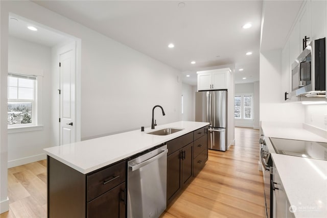 kitchen with sink, appliances with stainless steel finishes, white cabinetry, a kitchen island with sink, and dark brown cabinets