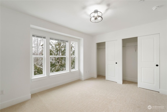 unfurnished bedroom featuring light colored carpet and multiple closets