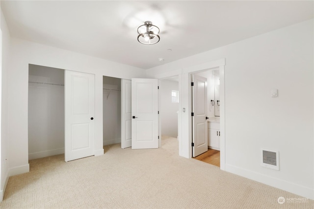 unfurnished bedroom with light colored carpet, ensuite bathroom, and two closets