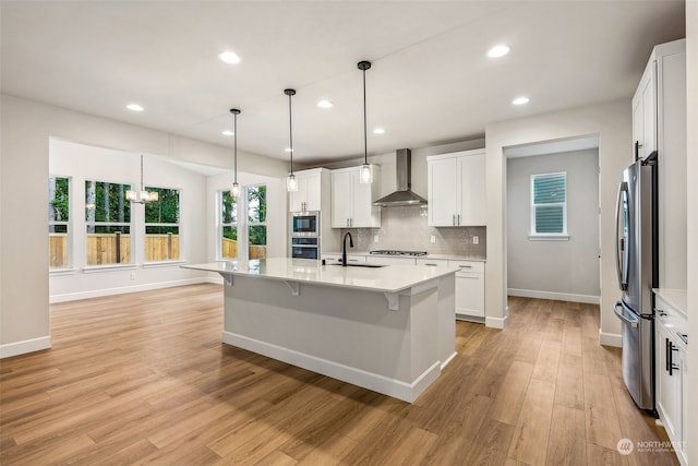 kitchen with wall chimney exhaust hood, white cabinetry, stainless steel appliances, and a center island with sink