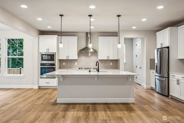 kitchen with wall chimney exhaust hood, white cabinetry, light hardwood / wood-style flooring, and stainless steel appliances