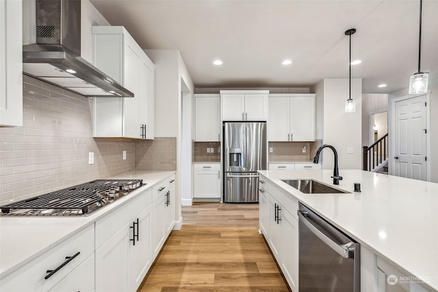 kitchen featuring white cabinets, stainless steel appliances, light hardwood / wood-style floors, wall chimney exhaust hood, and decorative light fixtures