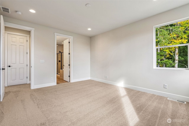 unfurnished bedroom featuring light colored carpet and ensuite bath