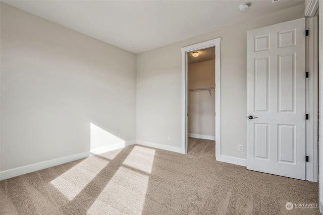 unfurnished bedroom with a spacious closet, a closet, and carpet floors