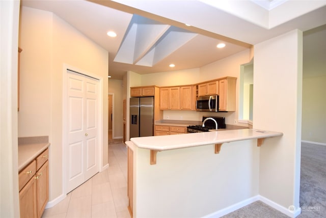 kitchen featuring light carpet, kitchen peninsula, a breakfast bar, light brown cabinetry, and stainless steel appliances