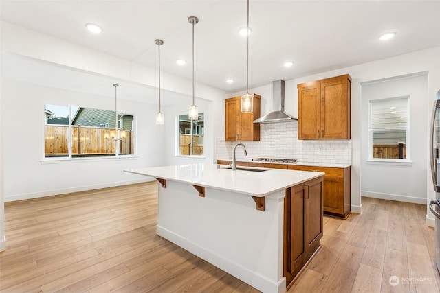 kitchen featuring a breakfast bar, sink, wall chimney exhaust hood, and an island with sink