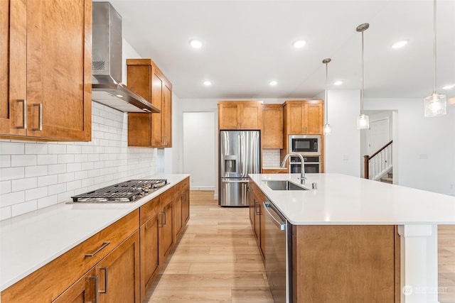 kitchen with appliances with stainless steel finishes, decorative light fixtures, a center island with sink, and wall chimney exhaust hood