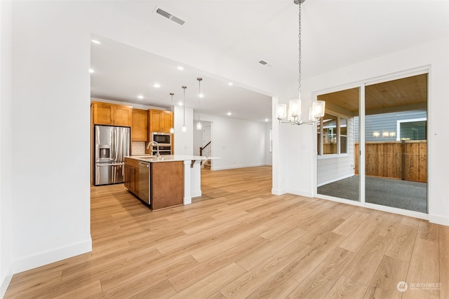 kitchen featuring appliances with stainless steel finishes, light wood-type flooring, hanging light fixtures, and a kitchen island with sink