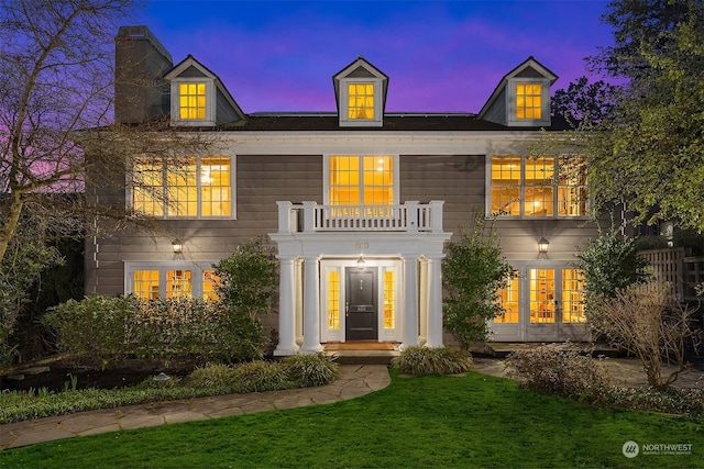 back house at dusk with french doors, a balcony, and a lawn