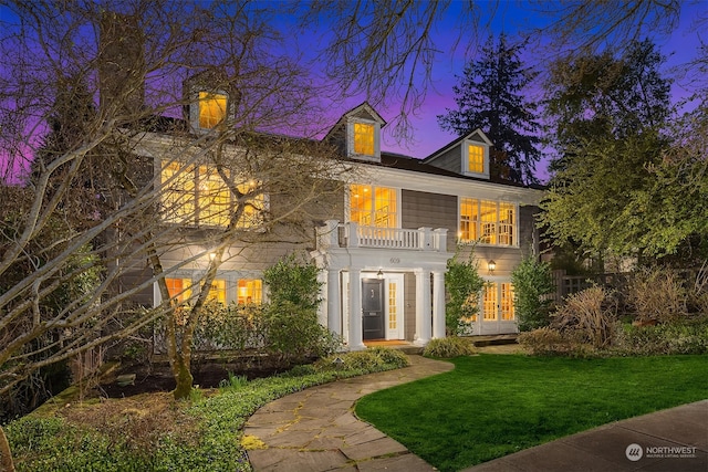 back house at dusk featuring a balcony and a lawn