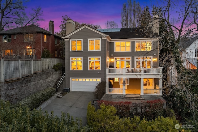 back house at dusk featuring a garage, a porch, and a balcony