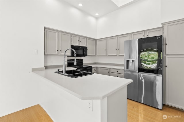 kitchen with a high ceiling, kitchen peninsula, black appliances, and light wood-type flooring