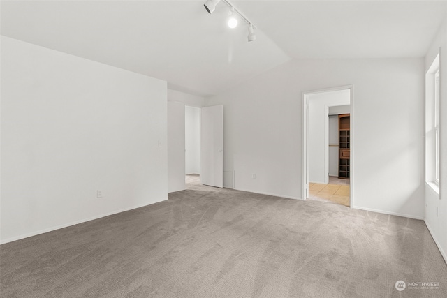 spare room featuring lofted ceiling, rail lighting, and light colored carpet