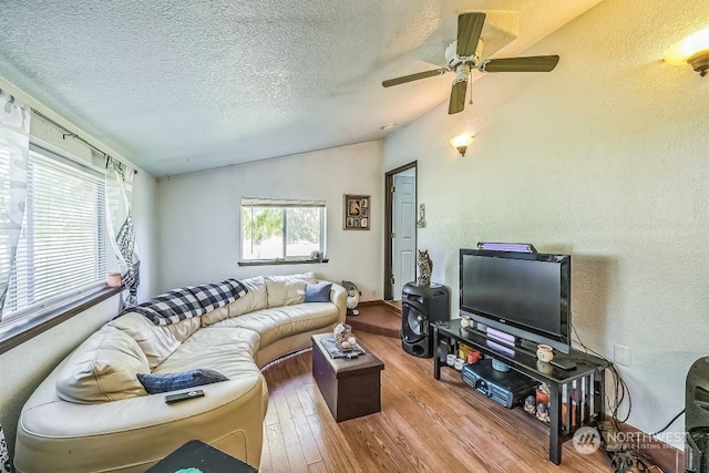 living room with a textured ceiling, ceiling fan, wood-type flooring, and vaulted ceiling