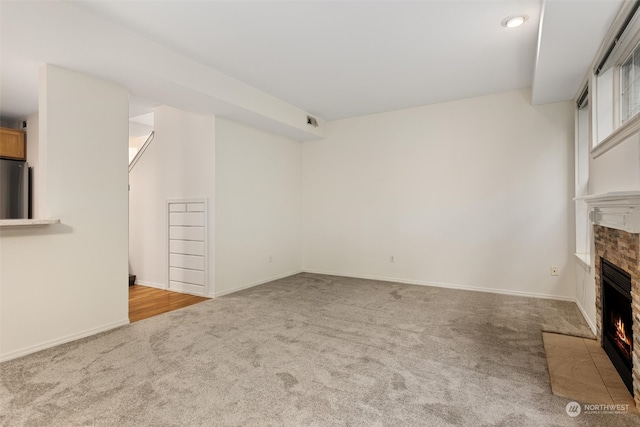 unfurnished living room featuring a fireplace with flush hearth, baseboards, and carpet floors